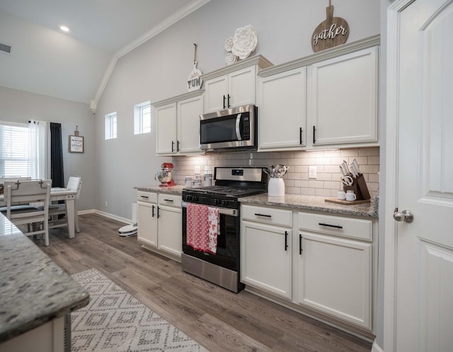 kitchen featuring appliances with stainless steel finishes, white cabinetry, lofted ceiling, decorative backsplash, and light stone counters