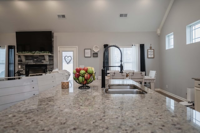 kitchen with light stone counters, lofted ceiling, a stone fireplace, and sink