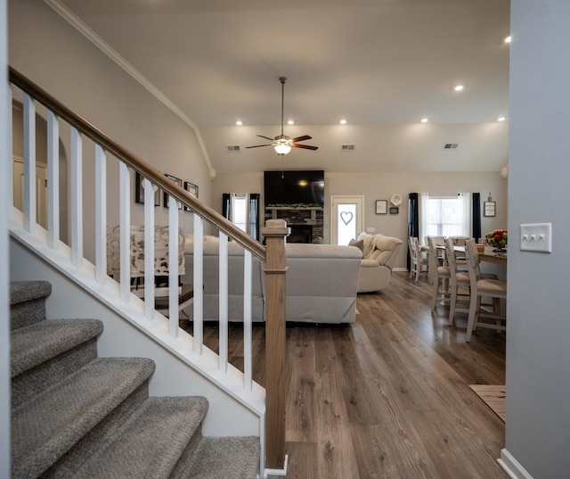 stairs featuring a fireplace, lofted ceiling, hardwood / wood-style flooring, ceiling fan, and crown molding