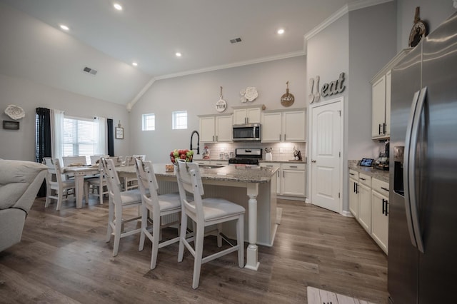 kitchen featuring white cabinetry, light stone countertops, stainless steel appliances, and a center island with sink