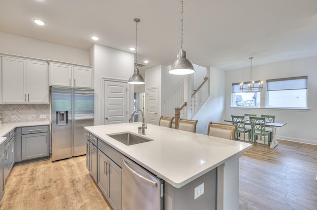 kitchen with sink, gray cabinetry, an island with sink, pendant lighting, and stainless steel appliances