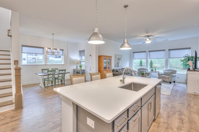 kitchen with sink, decorative light fixtures, light hardwood / wood-style flooring, stainless steel dishwasher, and a kitchen island with sink