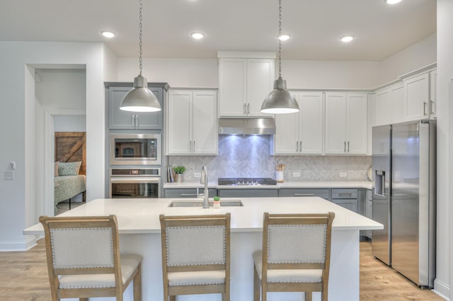 kitchen featuring an island with sink, appliances with stainless steel finishes, decorative light fixtures, and sink