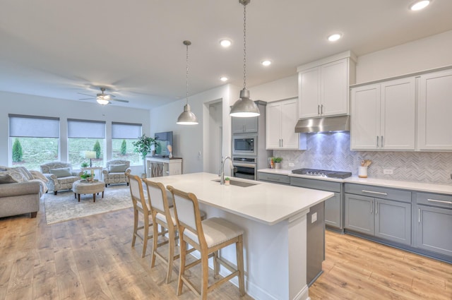 kitchen featuring a breakfast bar, decorative light fixtures, an island with sink, backsplash, and stainless steel appliances