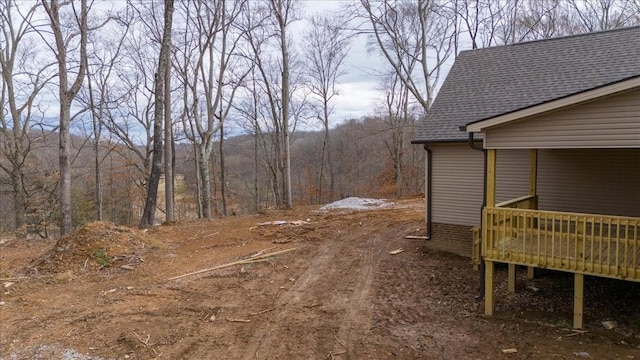 view of yard featuring a forest view, a deck, and dirt driveway