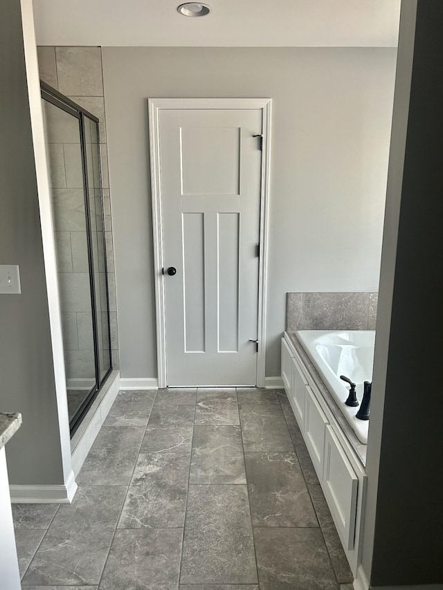 full bathroom featuring a bath, a stall shower, and baseboards