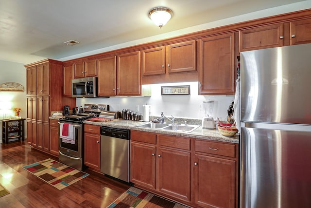 kitchen with light stone countertops, appliances with stainless steel finishes, sink, and dark wood-type flooring