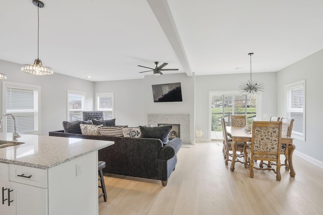 living room featuring beamed ceiling, sink, light hardwood / wood-style flooring, and a wealth of natural light