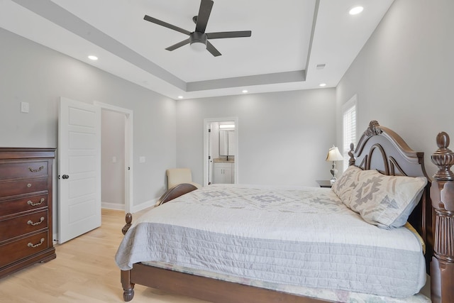 bedroom with ceiling fan, ensuite bath, a raised ceiling, and light hardwood / wood-style flooring