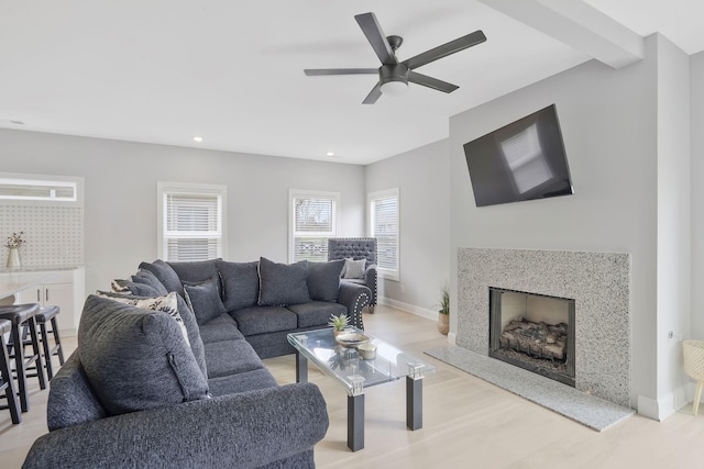 living room with beam ceiling, ceiling fan, a high end fireplace, and light hardwood / wood-style floors