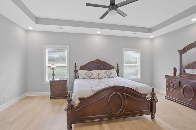 bedroom with a raised ceiling, light hardwood / wood-style floors, and multiple windows