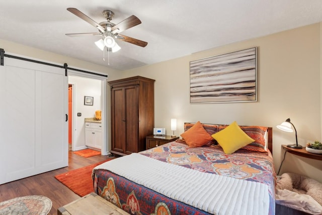 bedroom featuring ceiling fan, a barn door, connected bathroom, and dark hardwood / wood-style flooring