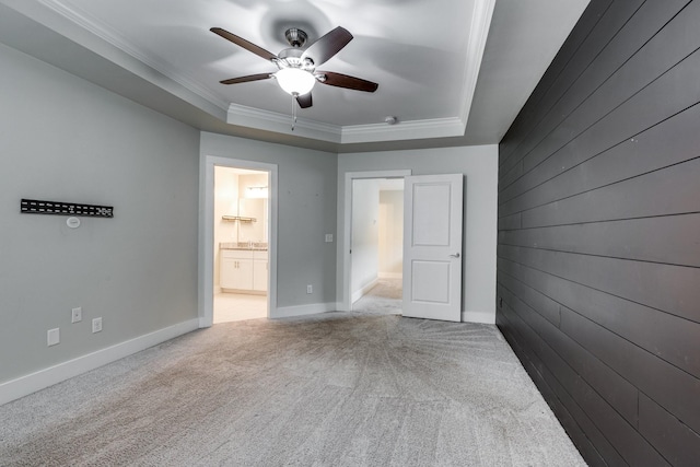 carpeted empty room with a raised ceiling, crown molding, ceiling fan, and wooden walls