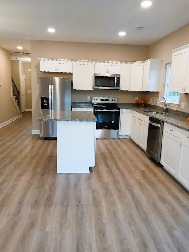 kitchen featuring white cabinets, appliances with stainless steel finishes, a center island, and dark stone counters