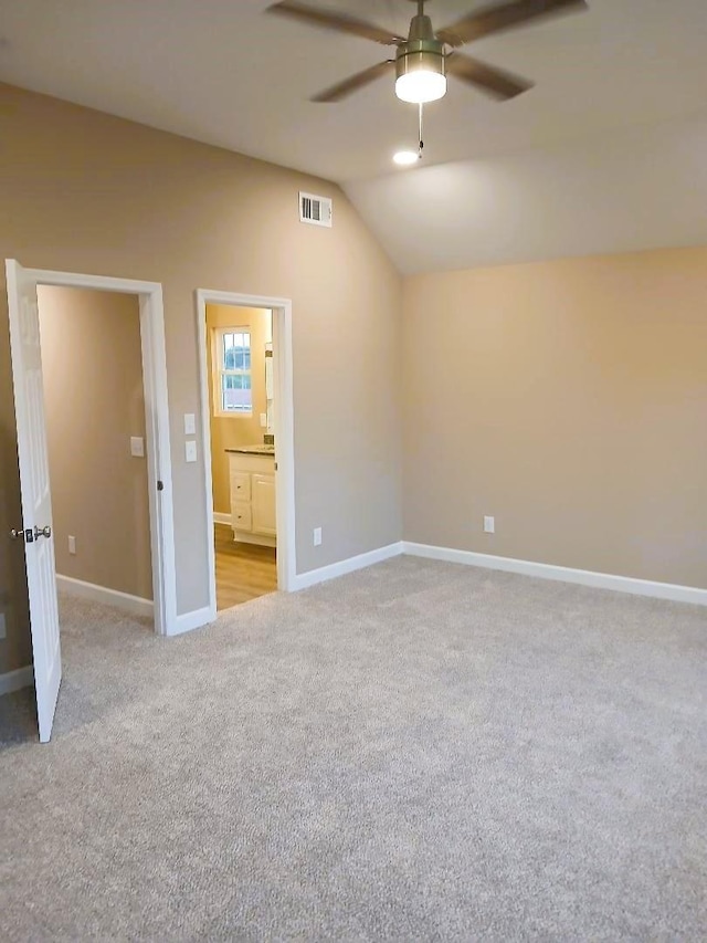 unfurnished bedroom featuring vaulted ceiling, light colored carpet, ceiling fan, and ensuite bath