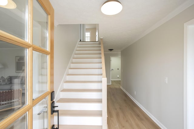 stairs featuring crown molding, a textured ceiling, and hardwood / wood-style flooring