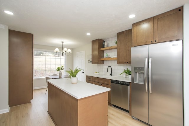 kitchen with sink, hanging light fixtures, stainless steel appliances, light hardwood / wood-style floors, and decorative backsplash