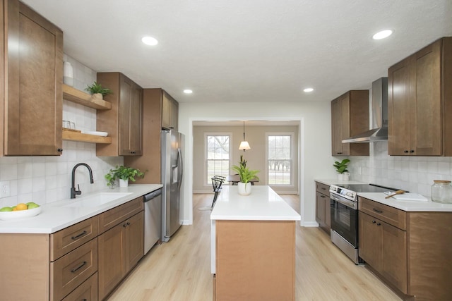 kitchen with sink, hanging light fixtures, light wood-type flooring, stainless steel appliances, and wall chimney range hood