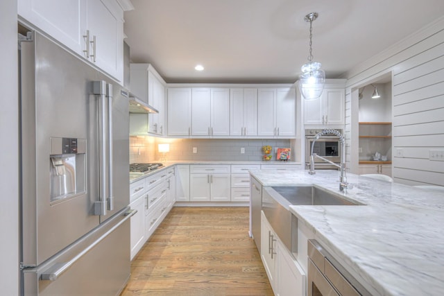 kitchen featuring pendant lighting, light hardwood / wood-style flooring, stainless steel appliances, light stone countertops, and white cabinets