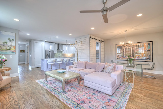 living room with a barn door, ceiling fan with notable chandelier, and light wood-type flooring