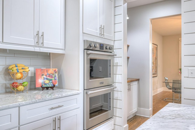 kitchen with white cabinetry, light stone counters, tasteful backsplash, and stainless steel double oven