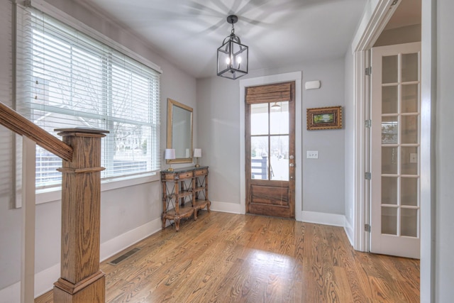 foyer entrance featuring wood-type flooring, a wealth of natural light, and an inviting chandelier