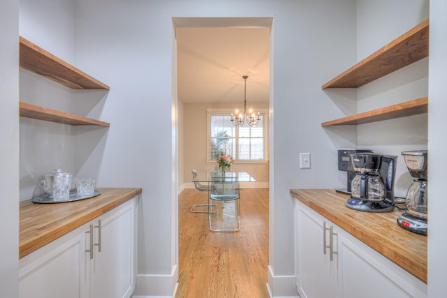 interior space featuring pendant lighting, butcher block counters, white cabinetry, a notable chandelier, and light hardwood / wood-style floors