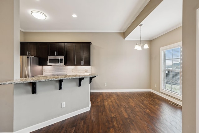 kitchen featuring pendant lighting, a breakfast bar area, backsplash, dark brown cabinets, and stainless steel appliances