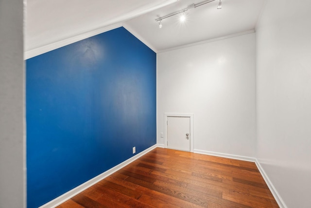 empty room with hardwood / wood-style flooring, vaulted ceiling, and track lighting