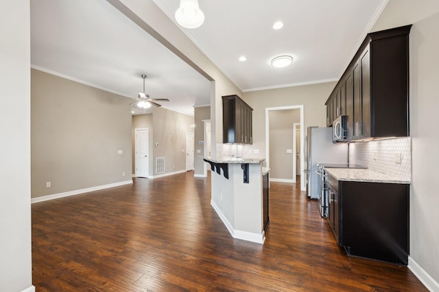 kitchen featuring ceiling fan, stainless steel appliances, a kitchen bar, and light stone countertops