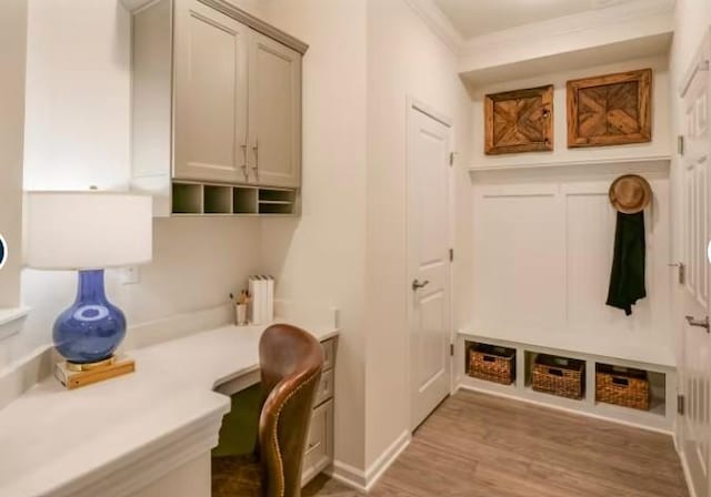 mudroom with crown molding, built in desk, and light wood-type flooring