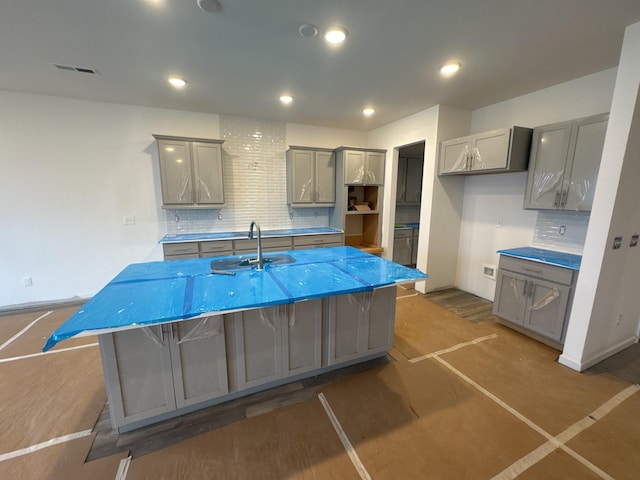 kitchen featuring gray cabinets, an island with sink, sink, and tasteful backsplash