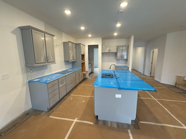 kitchen with sink, a kitchen island with sink, gray cabinetry, and decorative backsplash