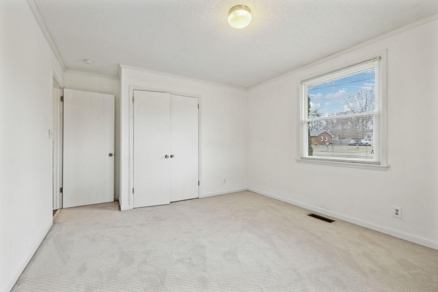 unfurnished bedroom with light carpet, ornamental molding, a closet, and a textured ceiling