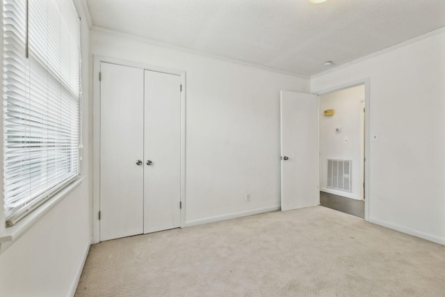 unfurnished bedroom featuring ornamental molding, light colored carpet, a closet, and a textured ceiling