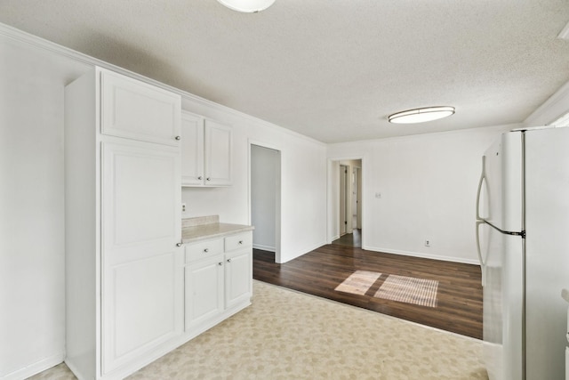 kitchen with hardwood / wood-style flooring, a textured ceiling, white cabinets, and white fridge