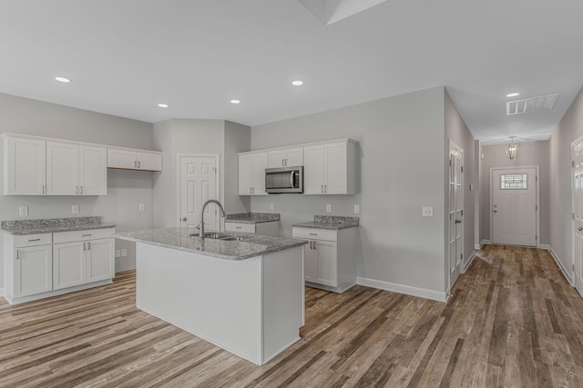 kitchen with a kitchen island with sink, sink, and white cabinets