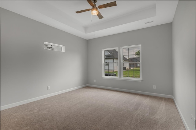 carpeted empty room with a raised ceiling and ceiling fan