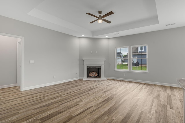 unfurnished living room featuring ceiling fan, light hardwood / wood-style floors, and a tray ceiling