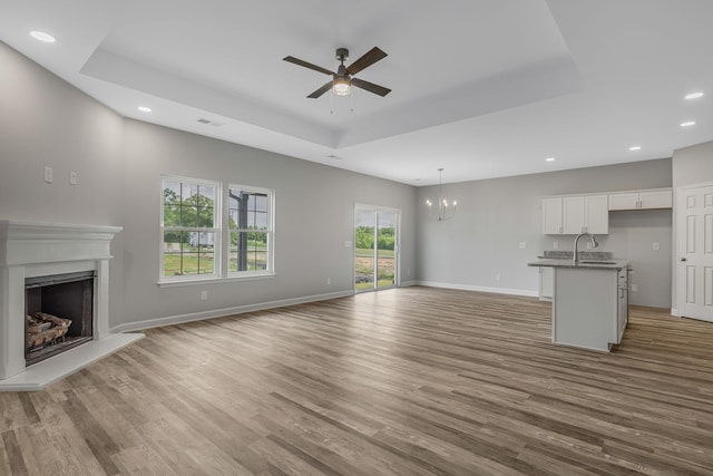 unfurnished living room with a raised ceiling, sink, hardwood / wood-style flooring, and ceiling fan with notable chandelier