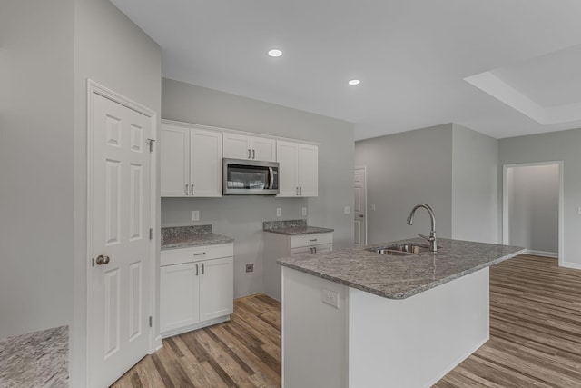 kitchen featuring sink, white cabinetry, light stone countertops, an island with sink, and light wood-type flooring