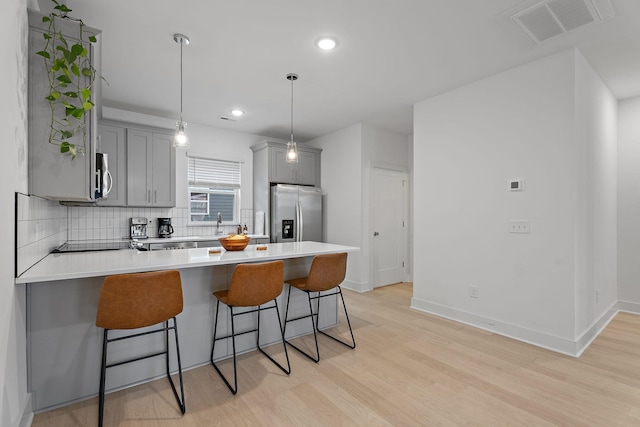 kitchen with stainless steel appliances, gray cabinets, a breakfast bar area, and decorative light fixtures