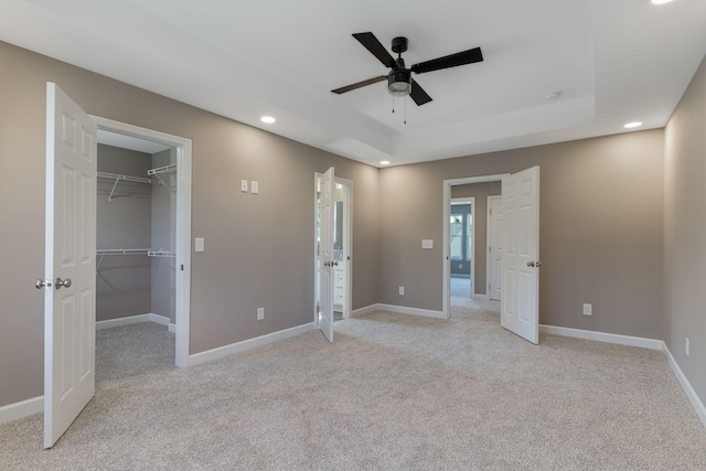 unfurnished bedroom featuring ceiling fan, a tray ceiling, light carpet, a walk in closet, and a closet