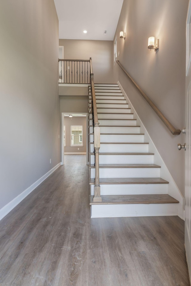 staircase with a towering ceiling and wood-type flooring