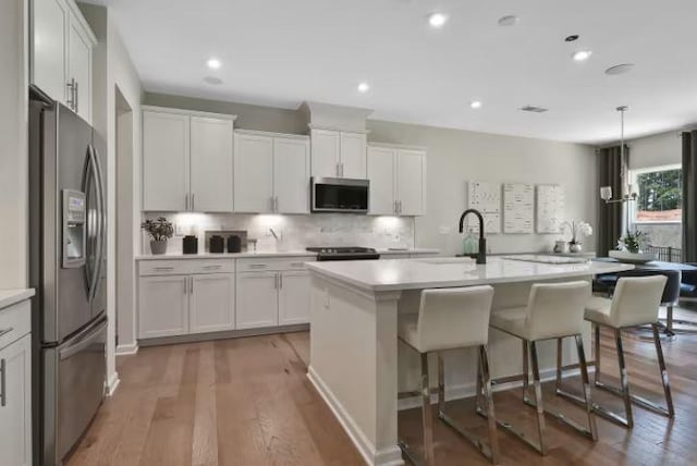 kitchen with sink, white cabinets, stainless steel appliances, a kitchen island with sink, and backsplash