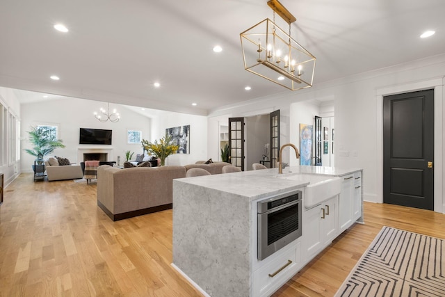 kitchen featuring white cabinetry, sink, hanging light fixtures, a kitchen island with sink, and light stone countertops