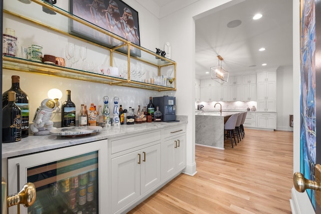 bar with wine cooler, tasteful backsplash, light hardwood / wood-style floors, and white cabinets