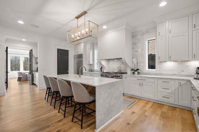 kitchen with stove, a kitchen breakfast bar, an island with sink, white cabinets, and built in fridge