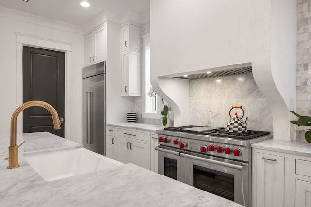 kitchen featuring sink, high quality appliances, light stone countertops, decorative backsplash, and white cabinets