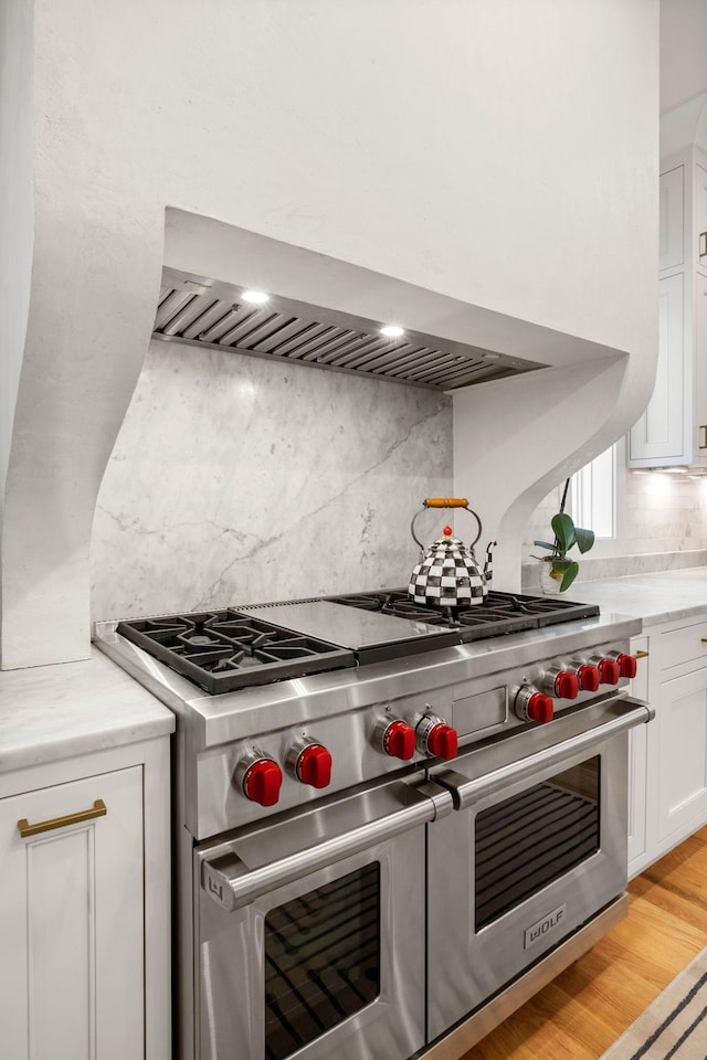 kitchen featuring tasteful backsplash, white cabinetry, light hardwood / wood-style flooring, range with two ovens, and wall chimney exhaust hood